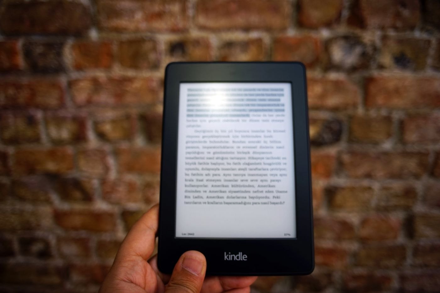Hand holding an e-reader in front of a brick wall